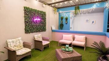 A cozy outdoor seating area with wicker furniture and a neon sign.