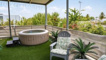A rooftop terrace with a hot tub, a chair, and a small table.