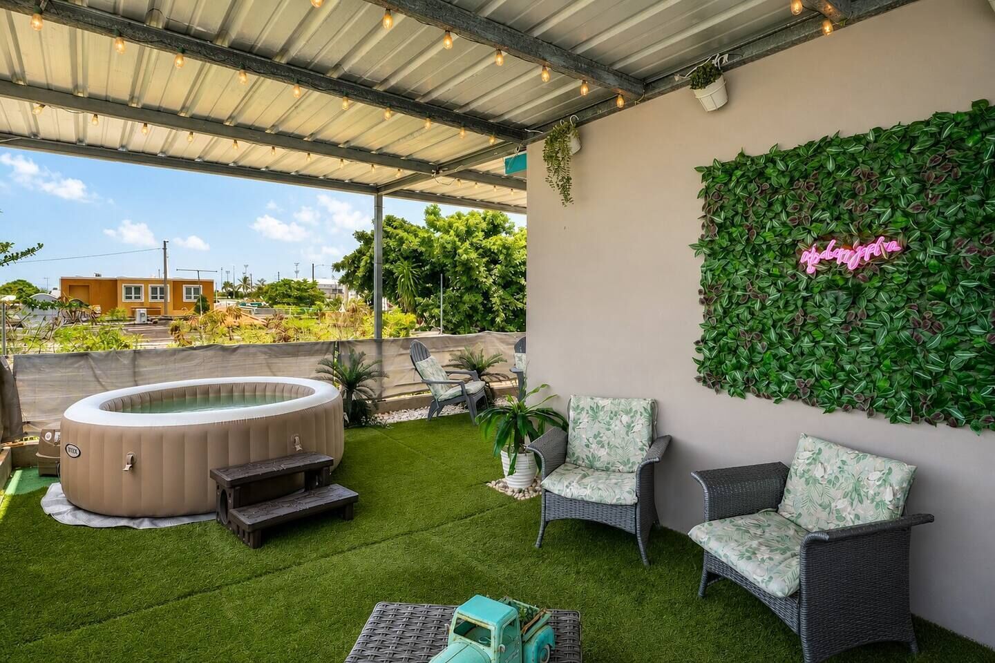 Un patio exterior con un jacuzzi, césped artificial, mobiliario de mimbre y una pared verde vertical.