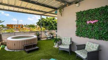 Un patio exterior con un jacuzzi, césped artificial, mobiliario de mimbre y una pared verde vertical.