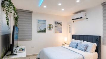 A bedroom with a bed, a TV, wall-mounted air conditioning, and artwork.