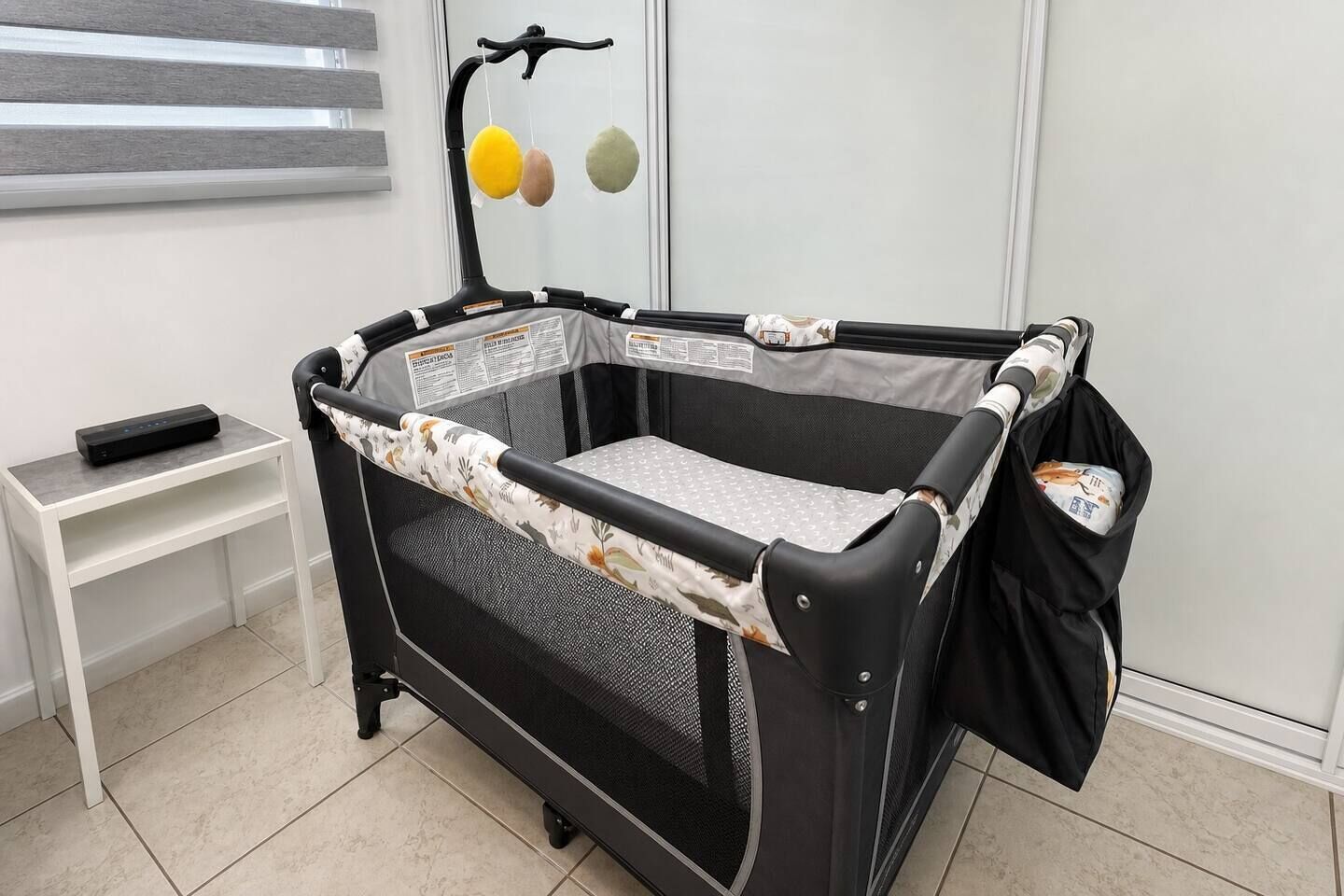 A baby playpen with a mesh floor, a padded side panel, and a hanging toy.