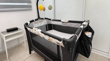 A baby playpen with a mesh floor, a padded side panel, and a hanging toy.