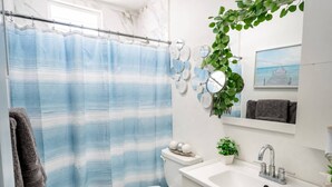 Ein Badezimmer mit Duschvorhang, Toilette, Waschbecken, Spiegel und einer Pflanze.
