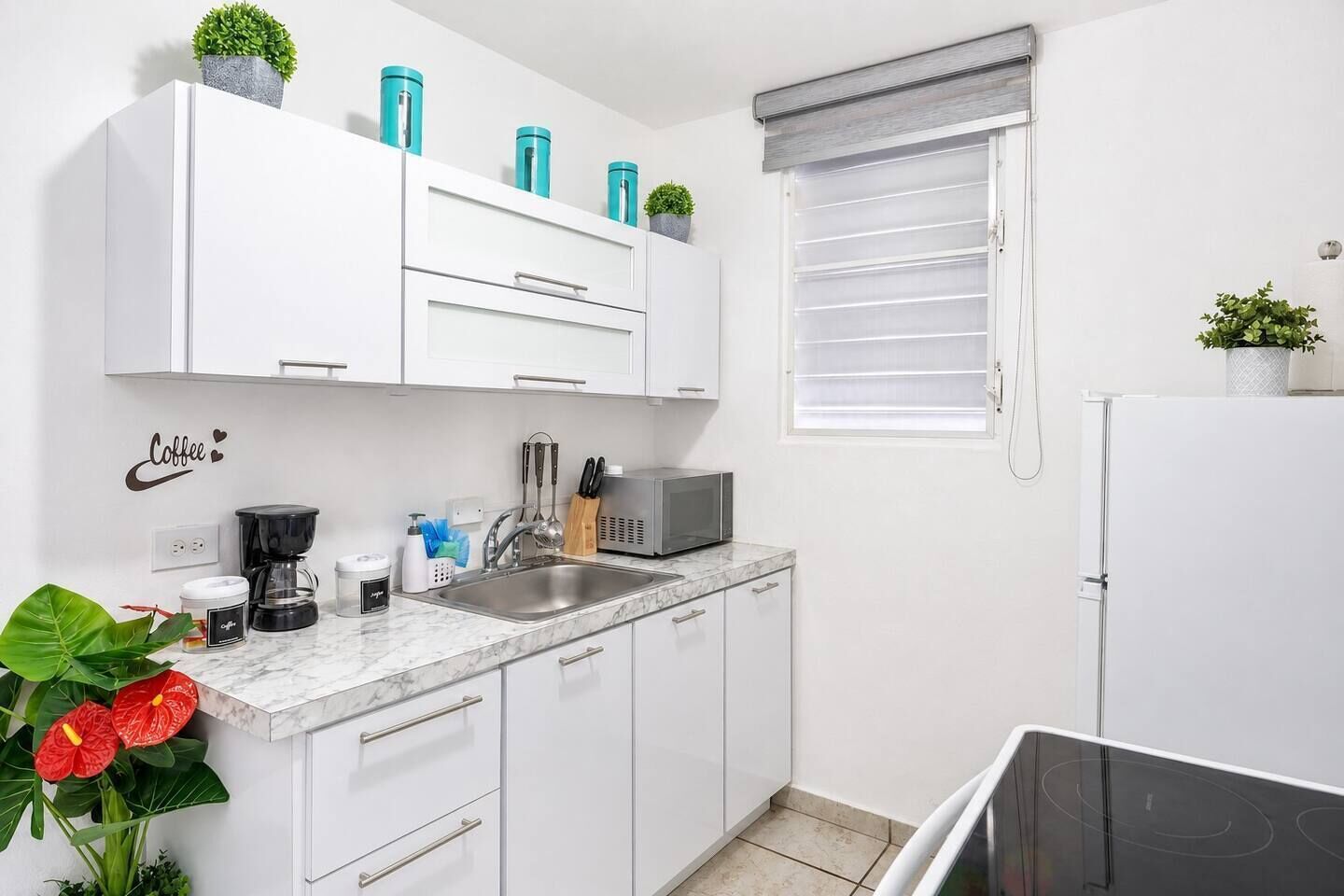 Una cucina moderna con mobili bianchi, un lavello, un forno a microonde e un piano cottura.