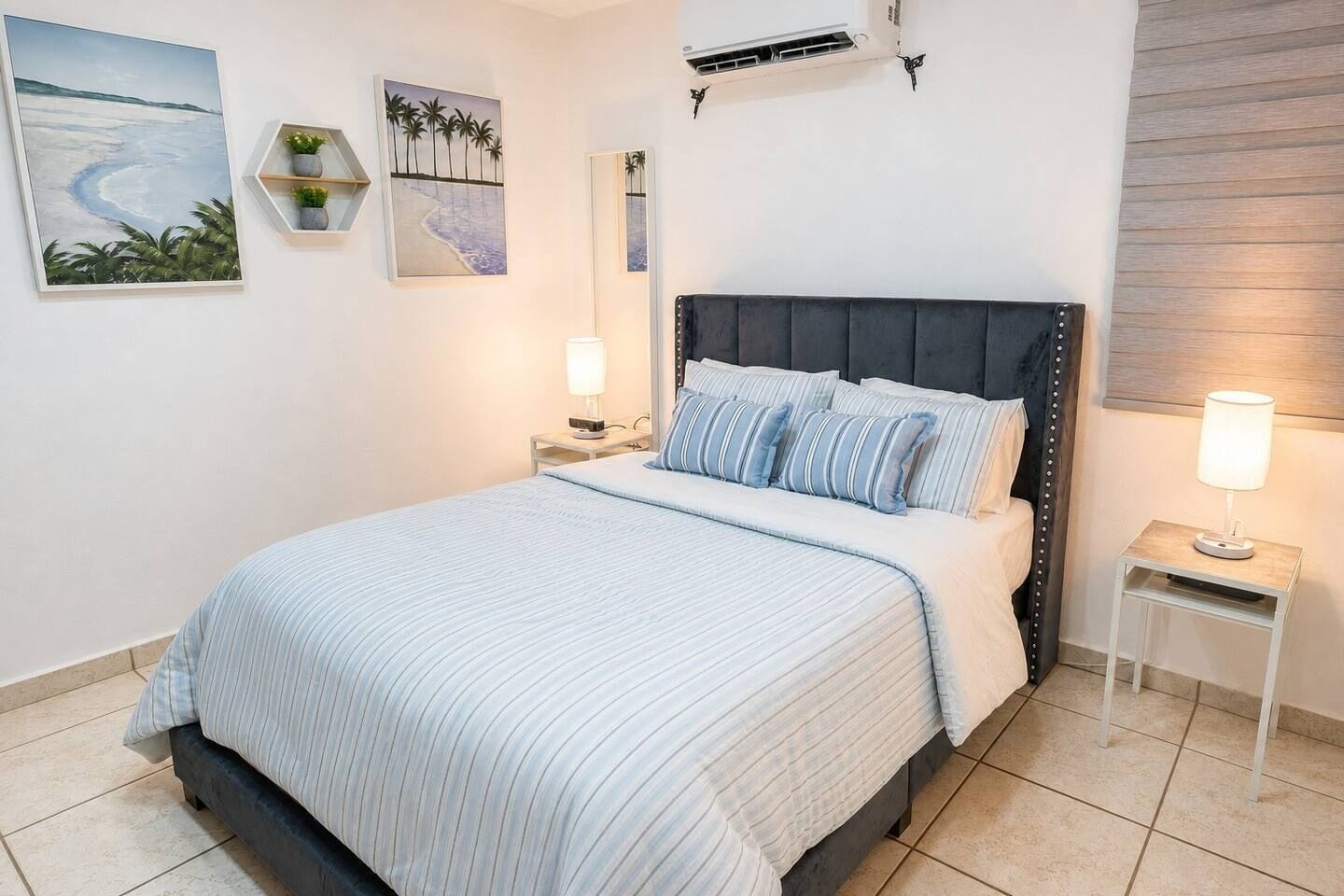 Een slaapkamer met een bed, nachtkastjes, airconditioning aan de muur en kunstwerk.