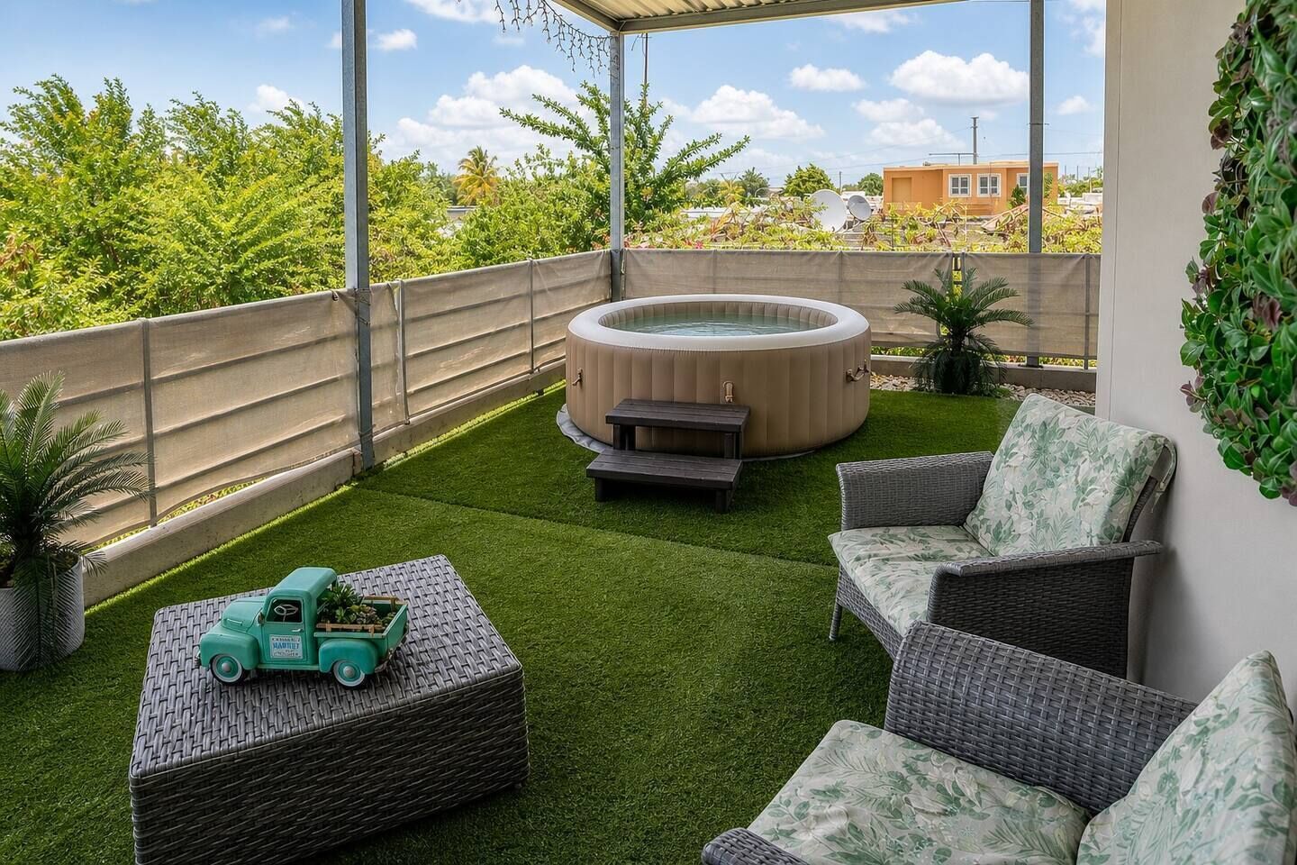 Ein überdachter Patio-Bereich mit Kunstgrasanlage, Korbmöbeln, einem Whirlpool und einem Spielzeugauto.
