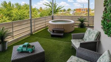 Ein überdachter Patio-Bereich mit Kunstgrasanlage, Korbmöbeln, einem Whirlpool und einem Spielzeugauto.