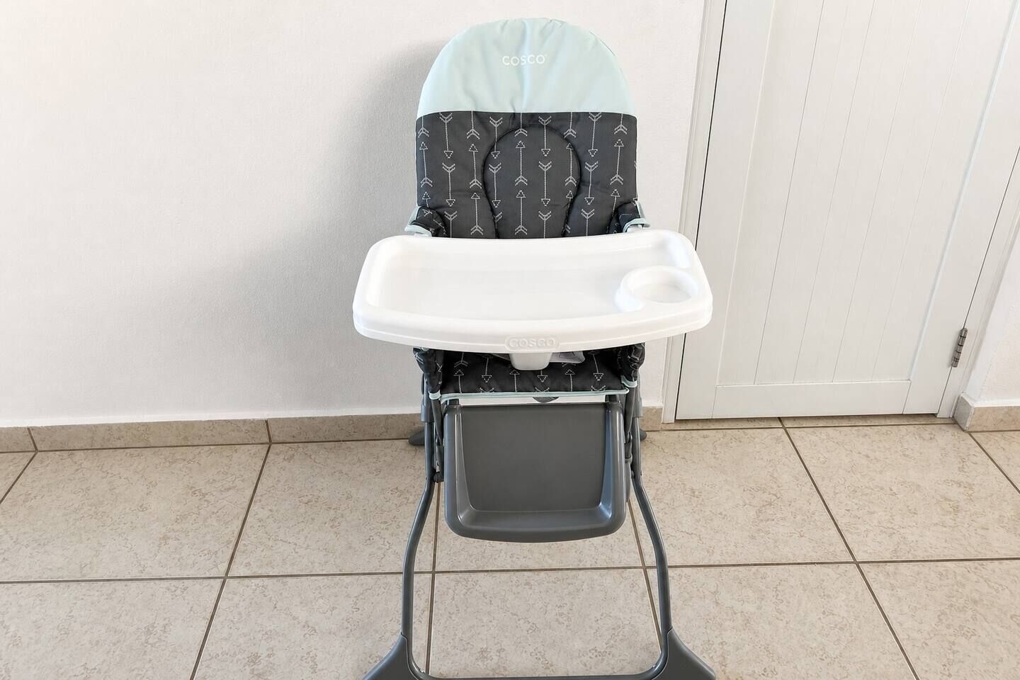 Uma cadeirinha de alimentação com mesa e almofada, sobre um piso de azulejos.