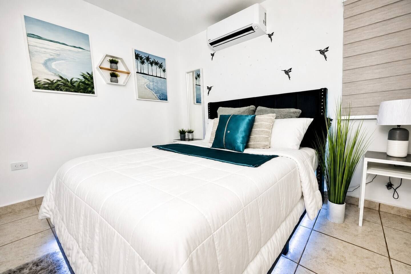 Un dormitorio moderno con una cama grande, una mesita de noche, una planta en maceta y cuadros en la pared.