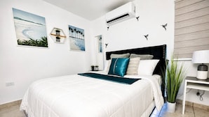 Ein modernes Schlafzimmer mit einem großen Bett, einem Nachttisch, einer Topfpflanze und Wandbildern.