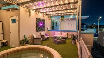 Terraza en la azotea con jacuzzi, zona de estar e iluminación con luces colgantes.