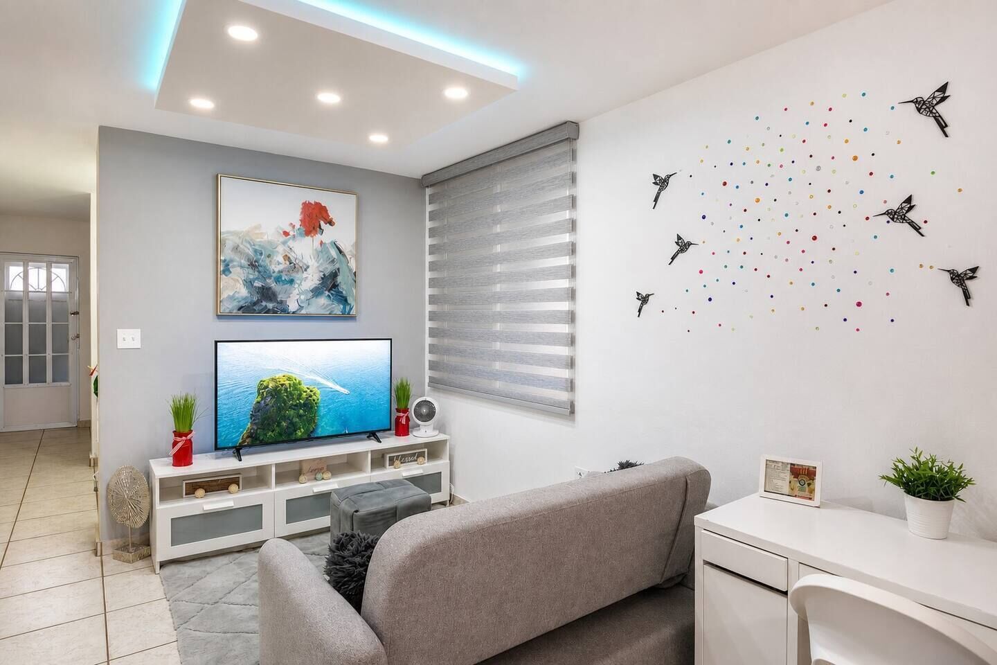 Un salon moderne avec un téléviseur à écran plat, un canapé gris et un coin repas avec une table blanche.