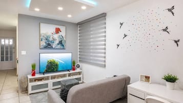 Un salon moderne avec un téléviseur à écran plat, un canapé gris et un coin repas avec une table blanche.