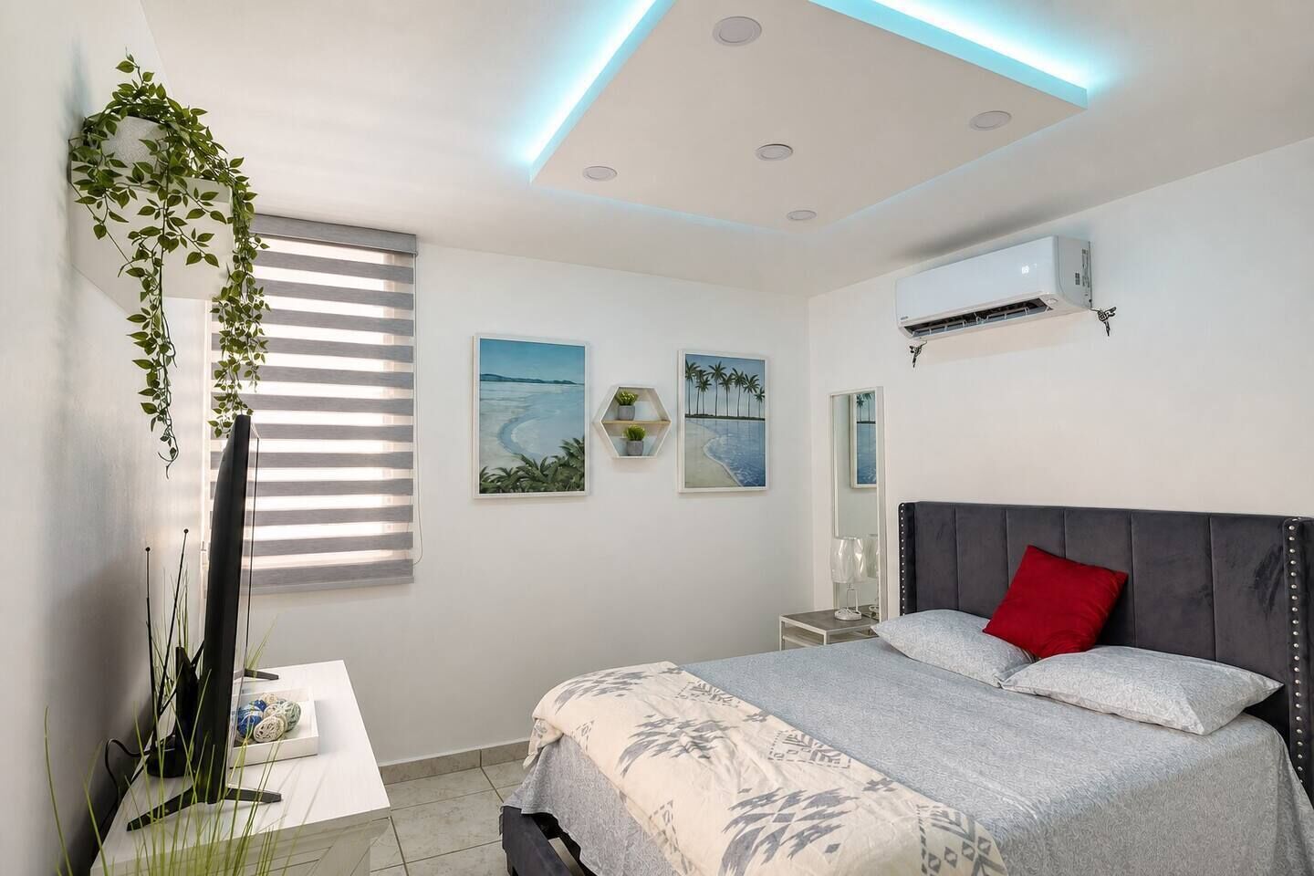 Une chambre moderne comprenant un lit, une table de chevet, un miroir et un climatiseur fixé au mur.