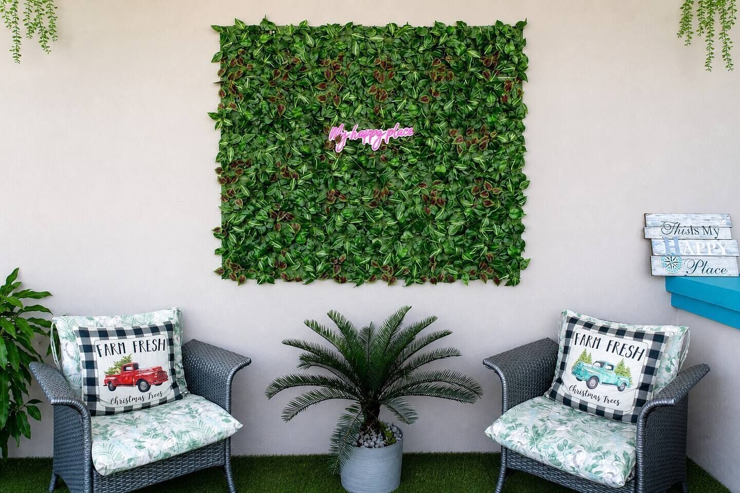 Une pièce avec deux fauteuils en osier, un sol recouvert d’un gazon synthétique vert, une décoration murale représentant du feuillage vert et une petite plante en pot.