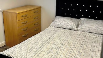 Ein Schlafzimmer mit einem Bett, einer Holzkommode und einer Deckenleuchte.