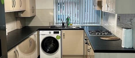 A compact kitchen with a washing machine, a sink, and a stove.