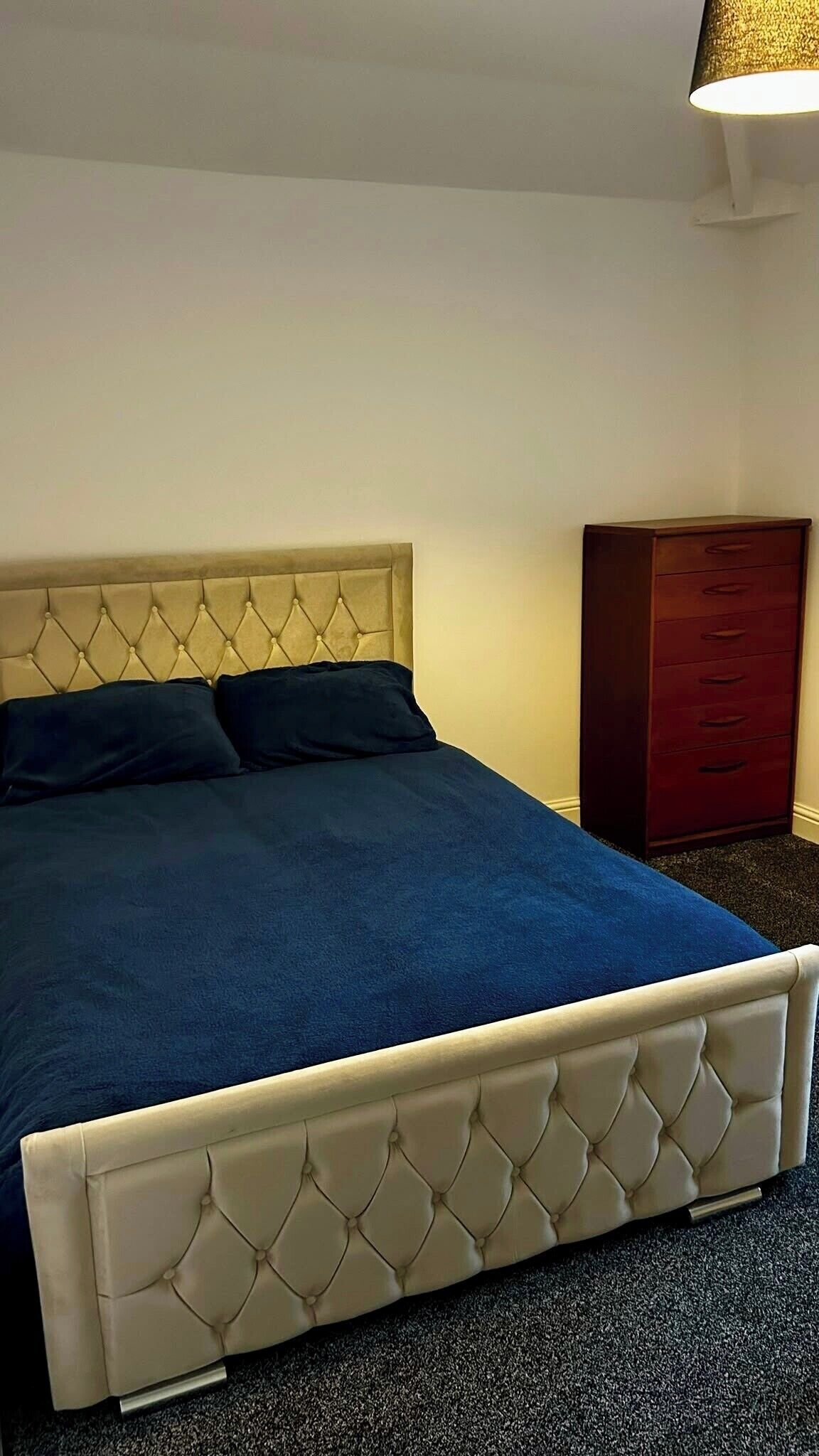 A bed with a tufted headboard, a dark blue bedspread, and a wooden nightstand with drawers.