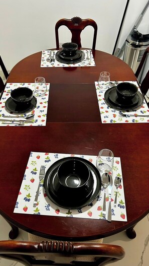 A dining table set with black plates, silverware, and glasses on a floral tablecloth.