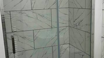 Eine gläserne Duschkabine mit Fliesen im Marmor-Design und einer blauen, rutschfesten Matte.