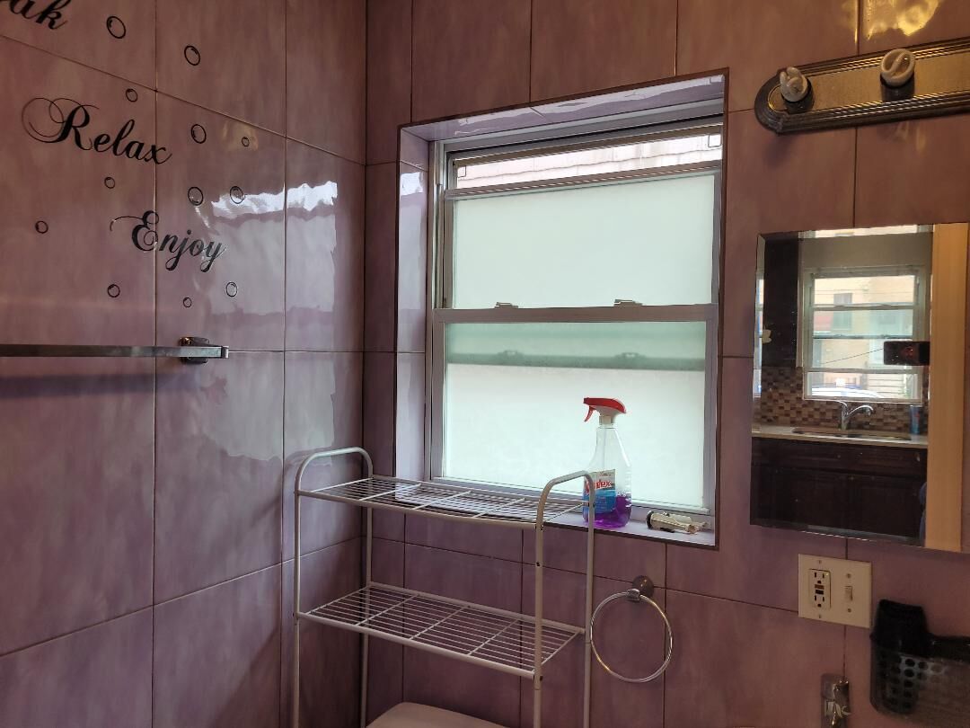 A bathroom with a window, a shelf with cleaning supplies, and a towel ring.