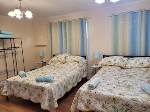 Ein Zimmer mit zwei Betten, darunter einem Etagenbett, einer Kristallleuchter, Vorhängen und einem kleinen Tisch mit einer Lampe.