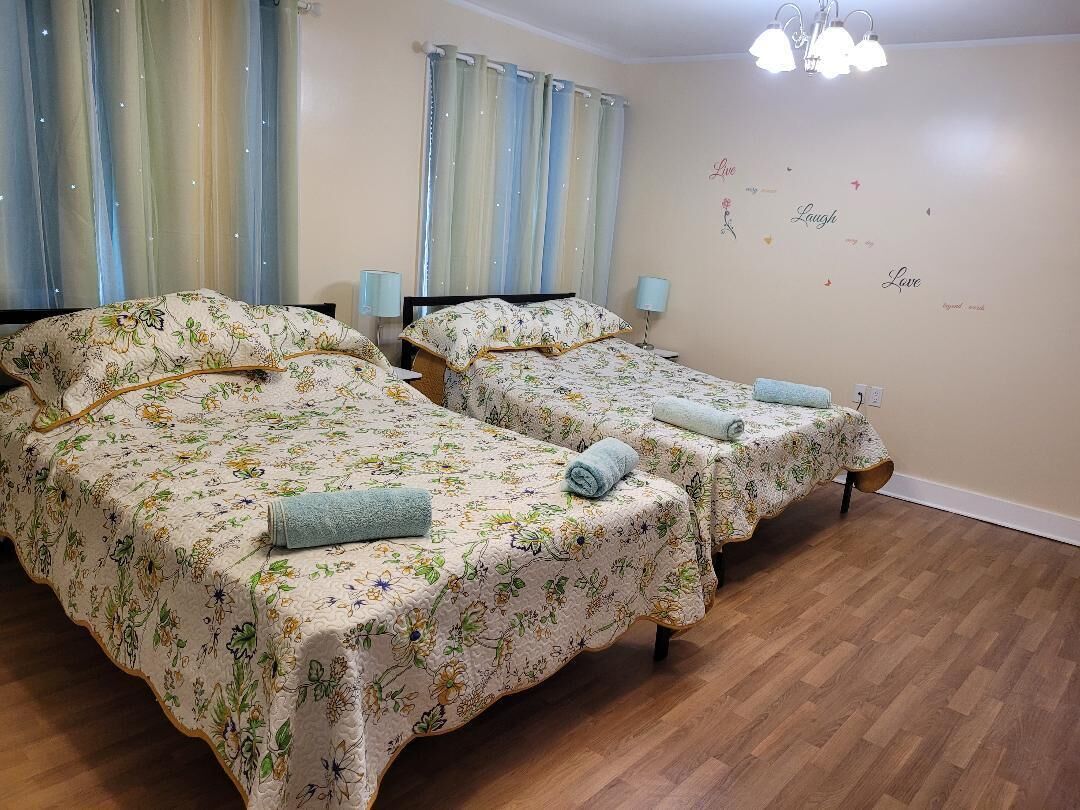 A room with two beds, each with floral bedding and towels, a chandelier, and a wall with decorative words.