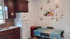 A kitchen with wooden cabinets, a refrigerator with decorative magnets, a dining table with chairs, and a wall decorated with food and kitchen-related stickers. - BEAUTIFUL 1 BEDROOM WITH BACKYARD (FOREST HILLS)