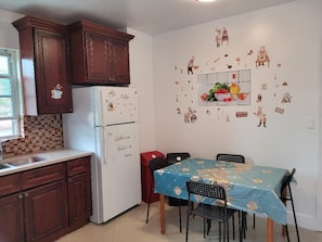 Eine Küche mit Holzausstattung, einem Kühlschrank mit Verzierungen und Magneten, einem Esstisch mit Stühlen sowie einer Wand, die mit Aufklebern zum Thema Essen und Küche dekoriert ist.