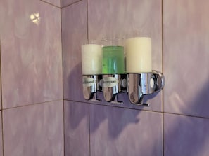 Ein Badezimmer mit Wandseifenspender und Ablage für drei Flaschen, auf denen 'Shampoo' steht.
