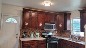 A kitchen with wooden cabinets, a microwave, a stove, and a window with a view. - BEAUTIFUL 1 BEDROOM WITH BACKYARD (FOREST HILLS)