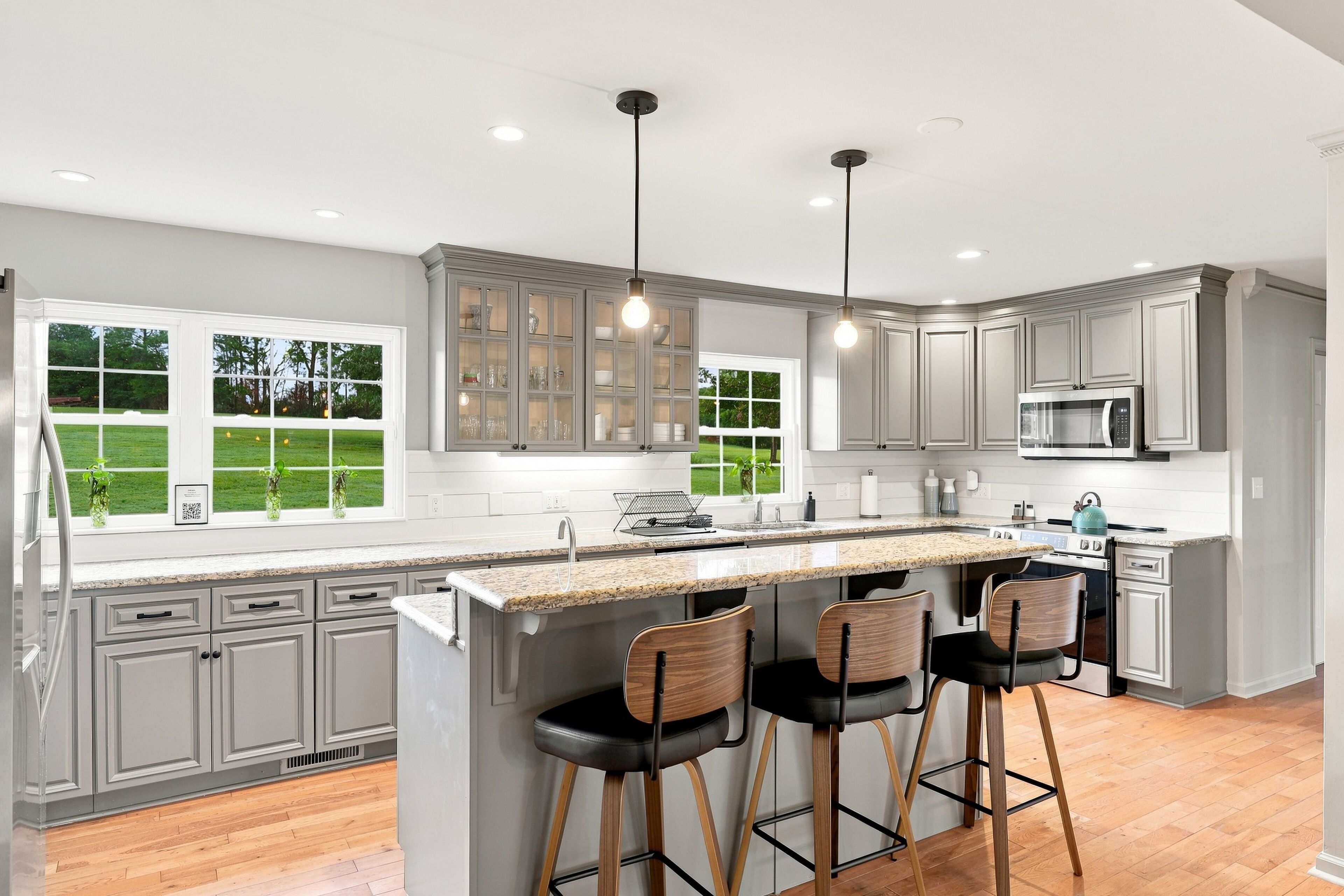 A modern kitchen with a large island, bar stools, and a view of the outdoors.