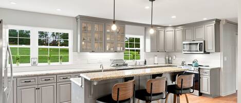 A modern kitchen with a large island, bar stools, and a view of the outdoors.