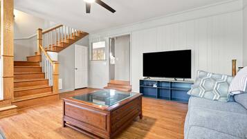 A living room with a wooden staircase, a glass coffee table, a flat-screen TV, and a grey sofa.