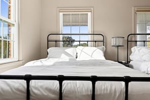 A bedroom with a single bed, a bedside table, a lamp, and a window.