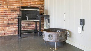 A brick wall, a black grill, and a metal pot on a concrete floor.