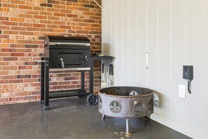 A brick wall, a black grill, and a metal pot on a concrete floor.
