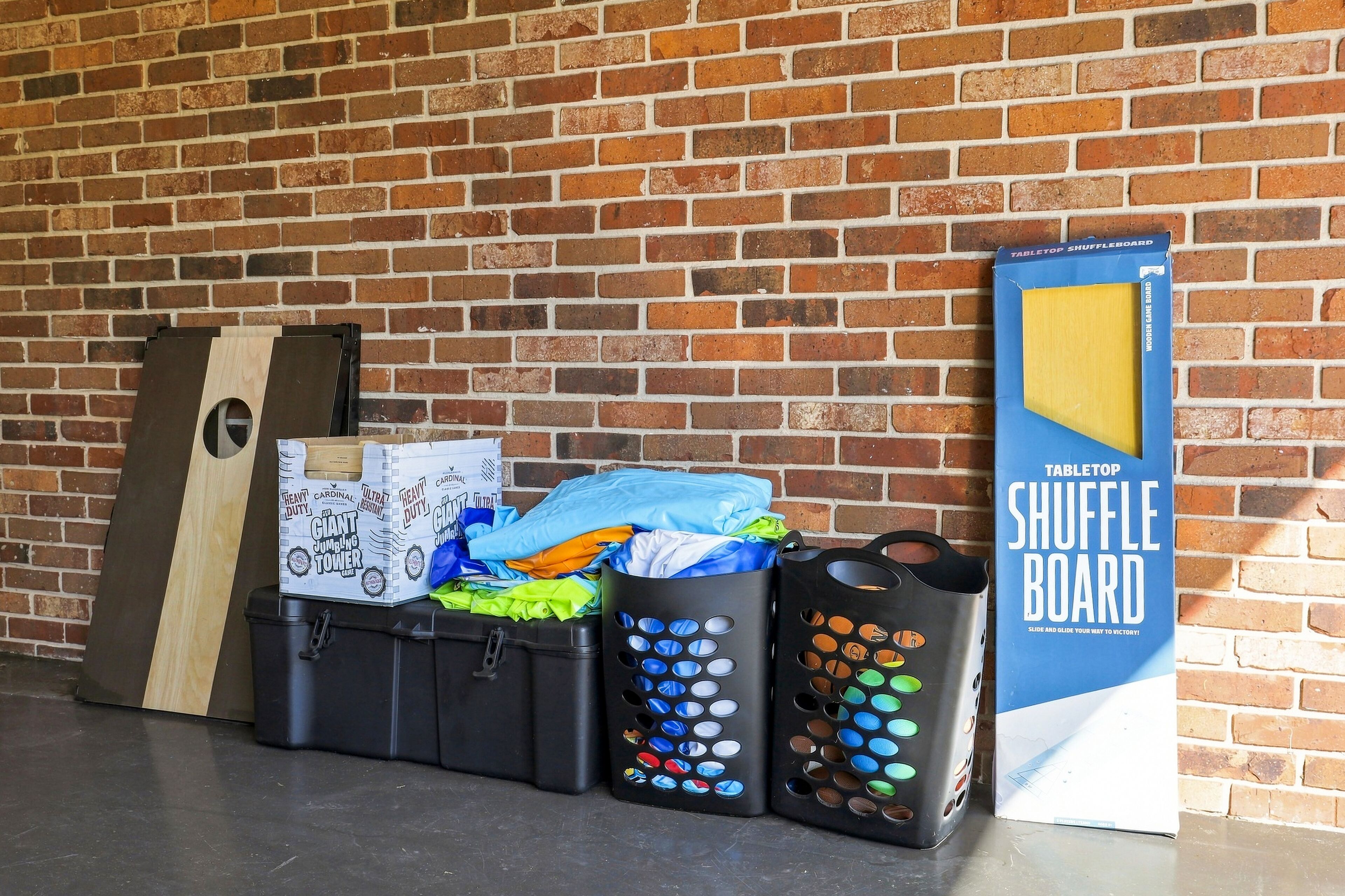 A brick wall with a wooden board game, a trash bin, and a table with folded clothes.