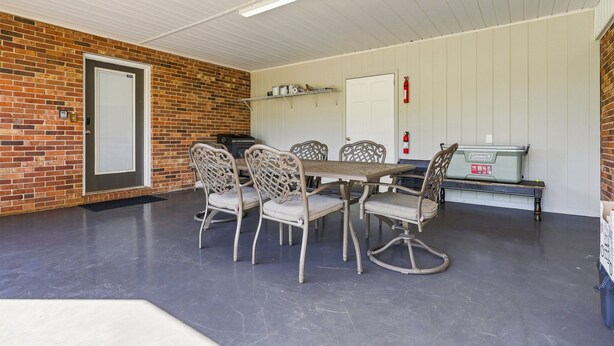 A covered outdoor dining area with a brick wall, a white ceiling, and a Coleman portable grill.