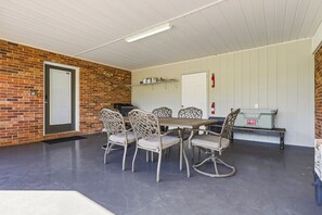 Un'area pranzo all'aperto coperta con un muro in mattoni, un soffitto bianco e una griglia portatile Coleman.