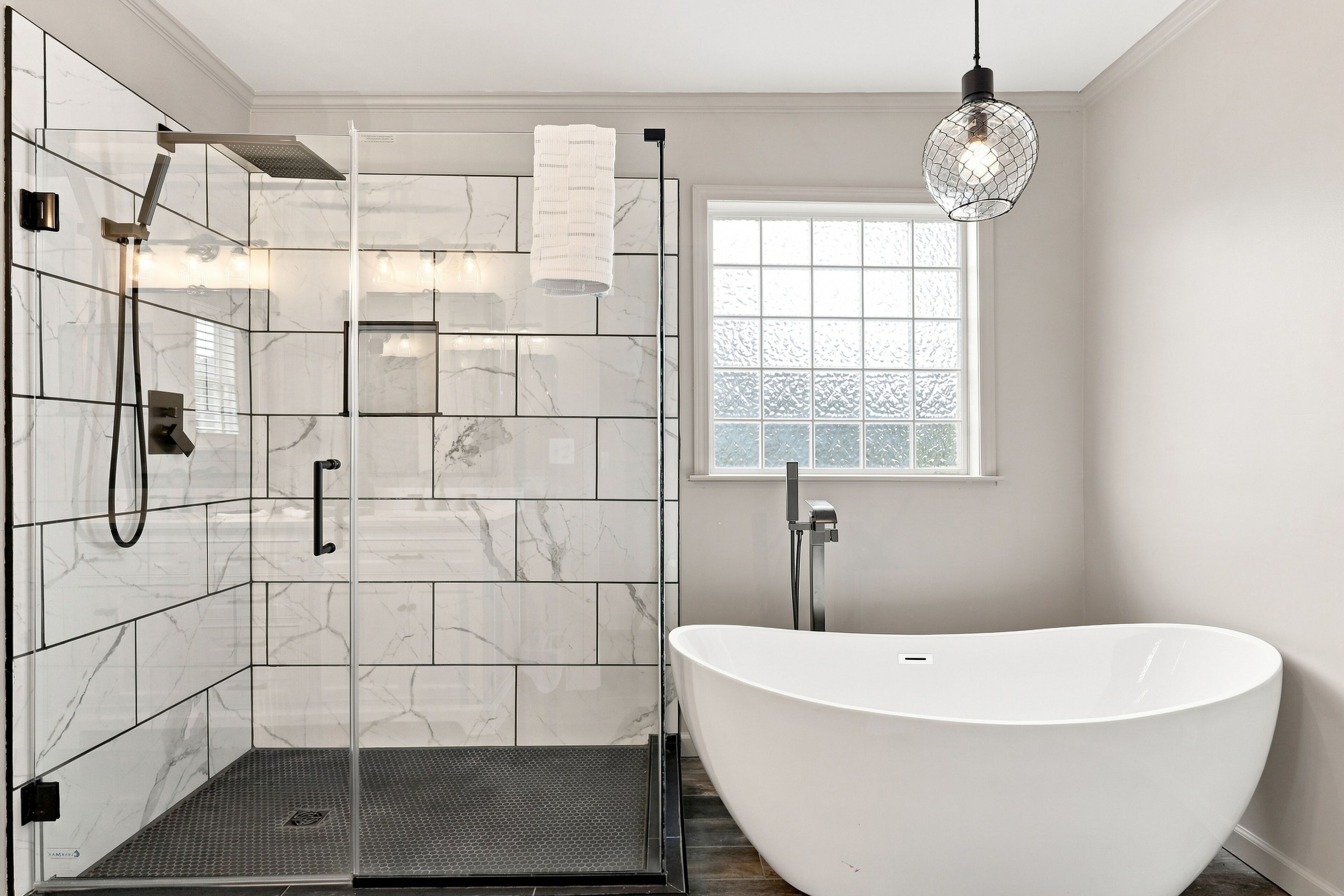 A modern bathroom with a glass-enclosed shower, a freestanding bathtub, and a window providing natural light.