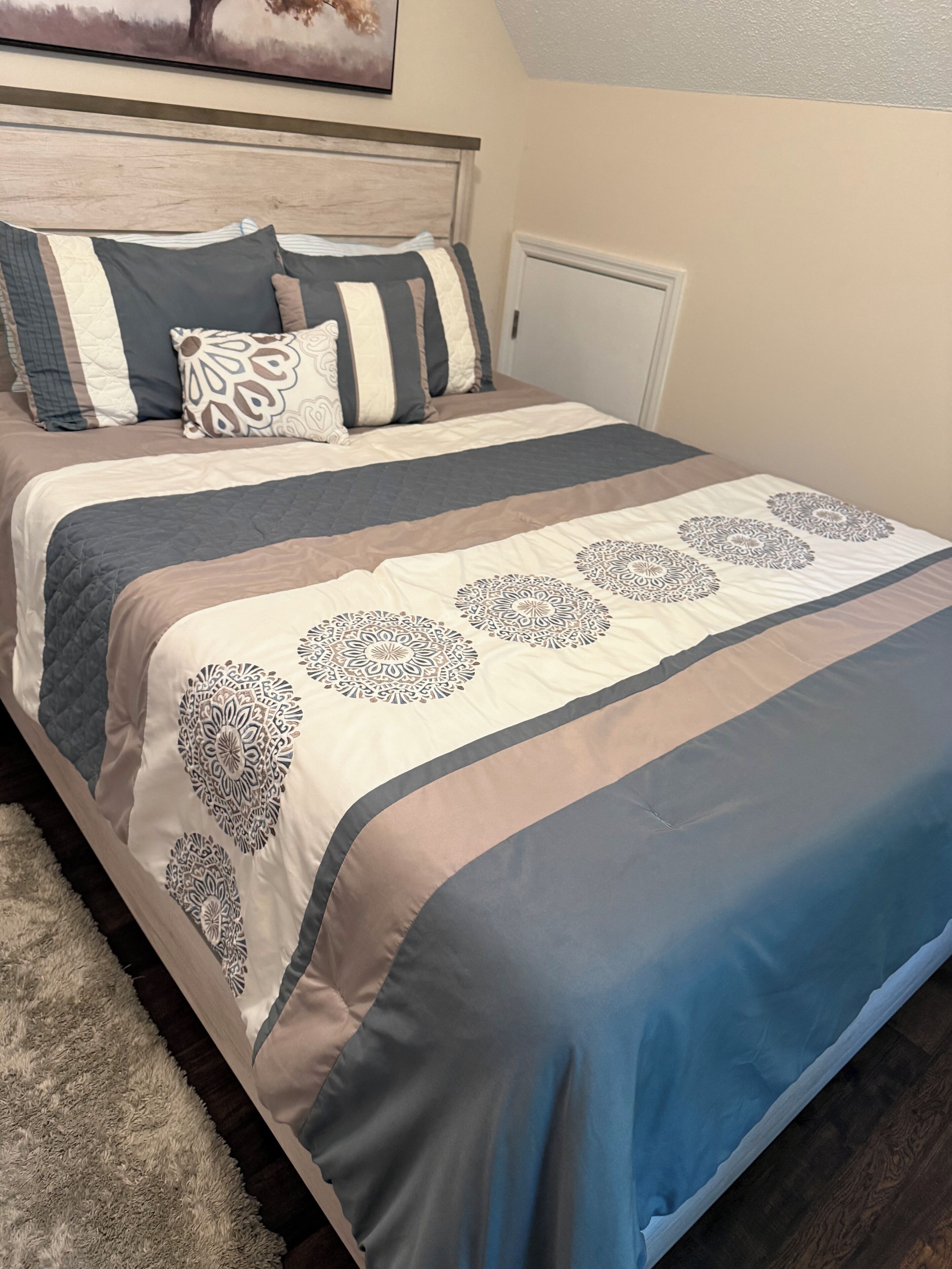 A neatly made bed with a patterned bedspread and pillows, a headboard, and a wall-mounted artwork.