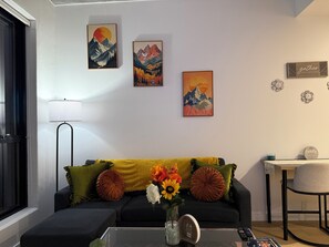 A living room with a sofa, a coffee table with a vase of flowers, and wall art. - The Sunset European Flat (Charlotte)