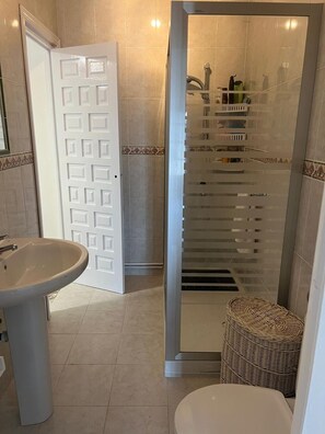A bathroom with a white sink, a toilet, a glass-enclosed shower, and a wicker basket. - Villa Mercedes Pool & 5 BDRM (Calpe)