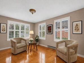 A room with two armchairs, a small table with a vase, and large windows with shutters.