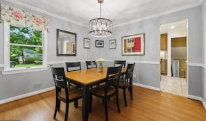 A dining room with a wooden table and chairs, a chandelier, and framed artwork on the walls.