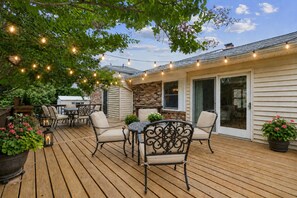 An outdoor deck with wooden flooring, outdoor furniture, string lights, and potted plants.