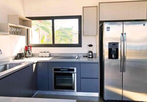 Eine moderne Küche mit eingebautem Ofen, einem Kühlschrank und einem Fenster mit Blick auf Grünflächen.