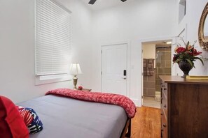 A bedroom with a bed, a dresser, a lamp, and a door leading to a bathroom. - Spacious 4-Bed NOLA Home, Pet-Friendly (New Orleans)